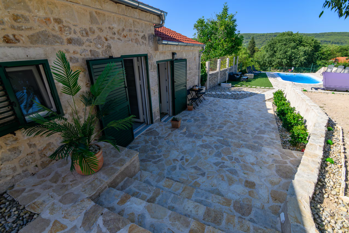 Stone patio and turquoise pool of Kameni Dvori under a bright Mediterranean sky